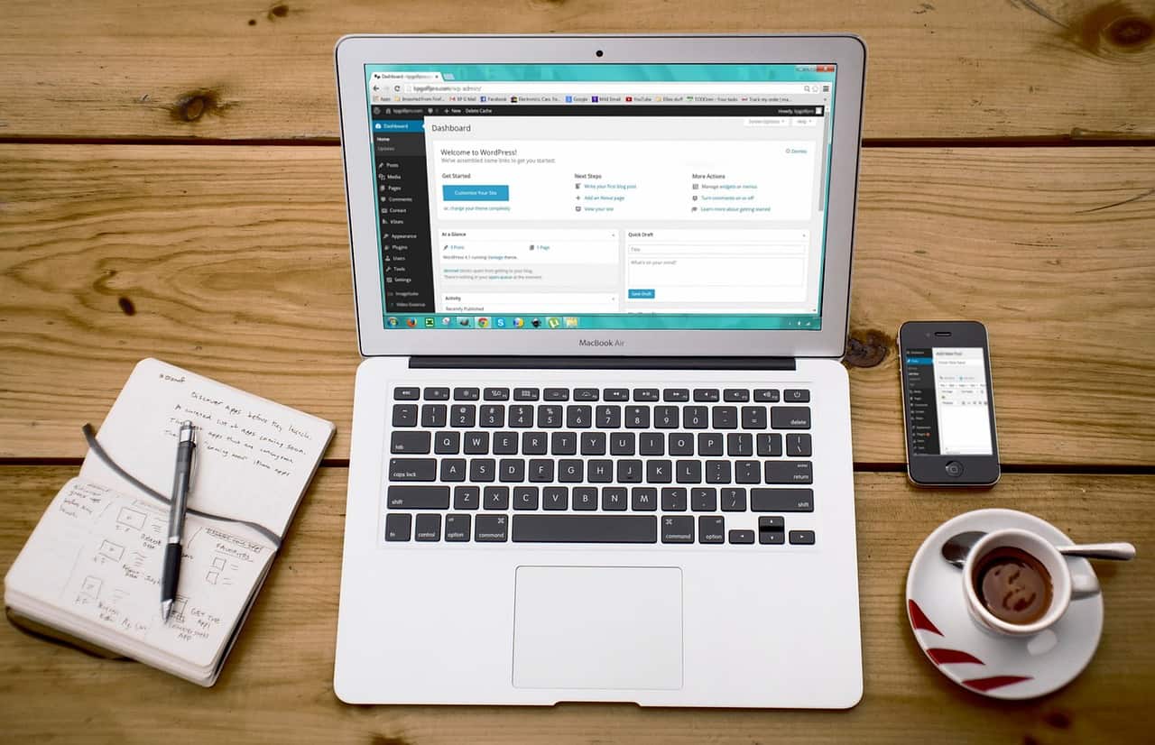 A laptop is sitting on a wooden table next to a cup of coffee and a phone.