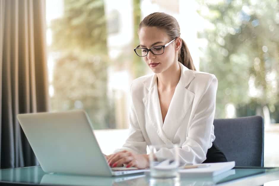 A woman in glasses is working on a laptop.