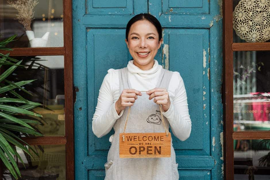 A woman in an apron holding a welcome sign in front of a blue door.