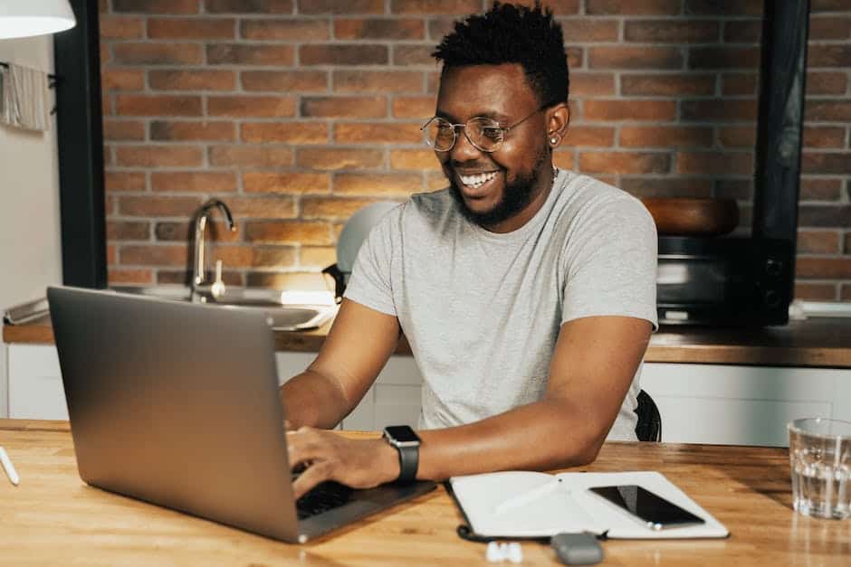 A black man sitting at a table working on a laptop.