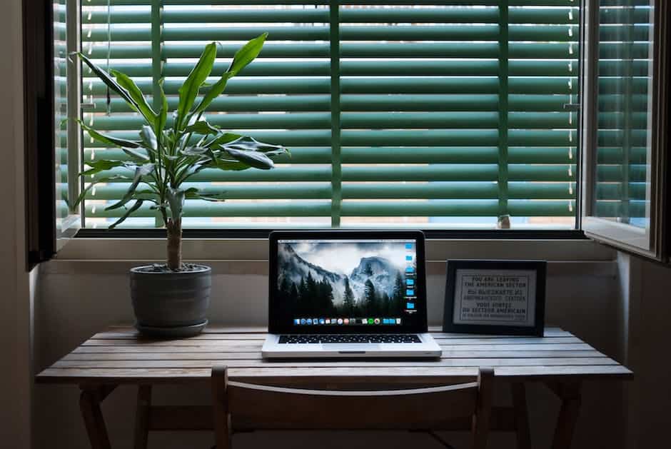 A laptop on a desk next to a window with green shutters.