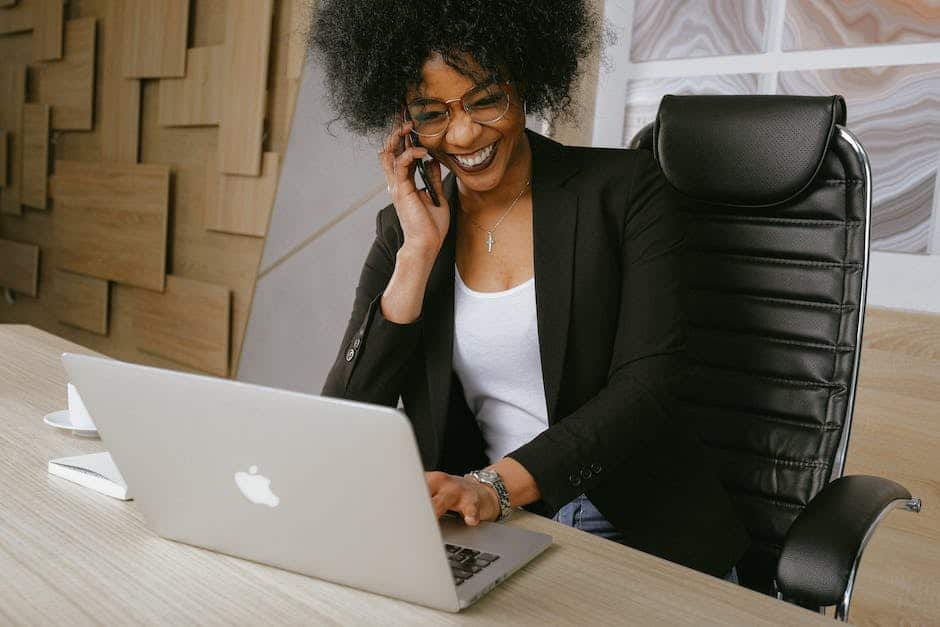 A black woman talking on the phone while sitting at a desk with a laptop.