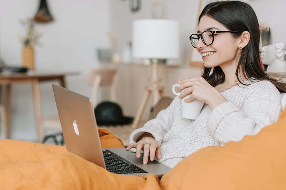 A woman sitting on a couch with a laptop and a cup of coffee.