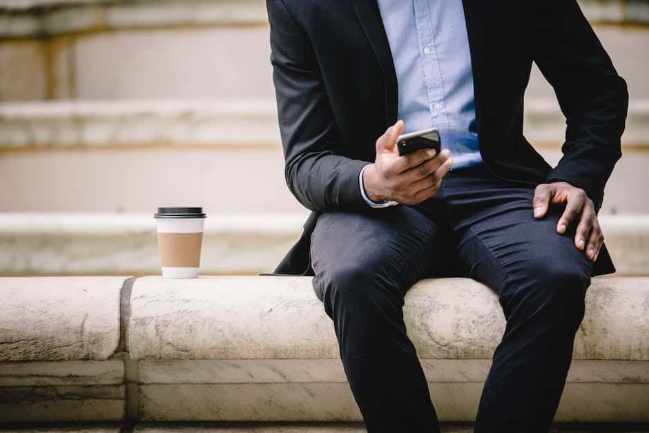A man in a suit sitting on a step while using his cell phone.