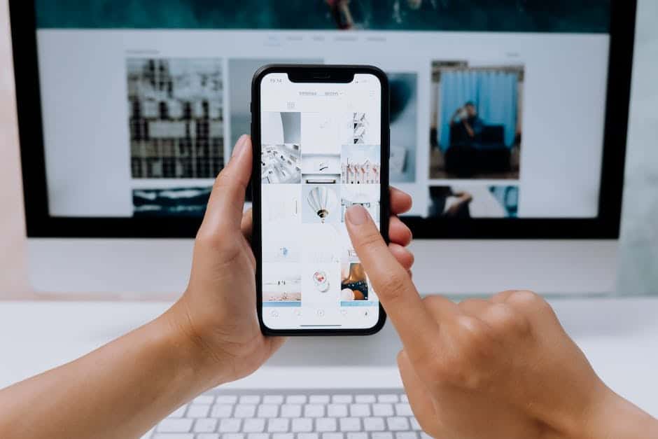 A person holding an iphone in front of a computer screen.