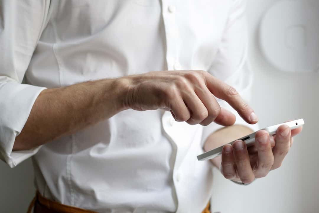 A man in a white shirt is holding a cell phone.