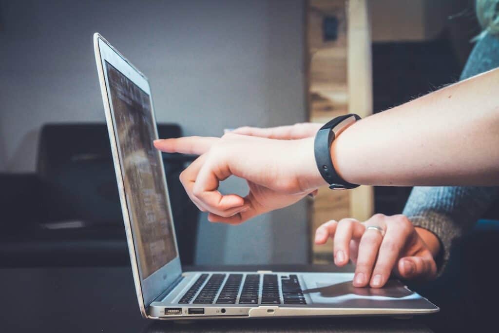 A person pointing at a laptop on a table.