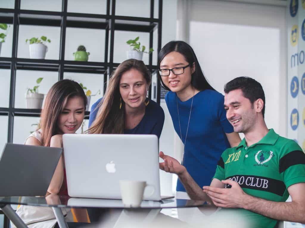 A group of people sitting around a table looking at a laptop.