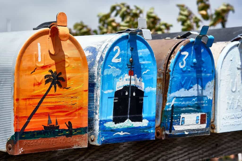 A row of painted mailboxes on a fence.