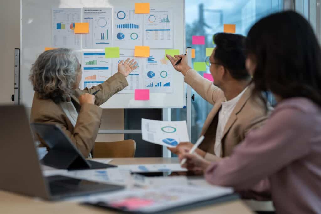 A group of business people at a meeting brainstorming effective B2B sales strategies for SaaS companies with sticky notes on a whiteboard.